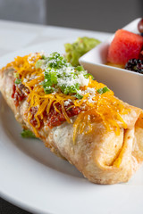 A view of a burrito on a plate, with a side bowl of fresh fruit, in a restaurant or kitchen setting.