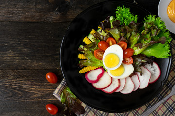 Fresh salad with boiled egg in black dish on wooden table, Tomato and Radish.