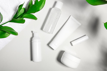Cosmetic products containers on gray light background. Face cream, nourishing mask jar with leaf shadows and white towel. Lip balm, shampoo, moisturizing face lotion and body cream. Organic skincare
