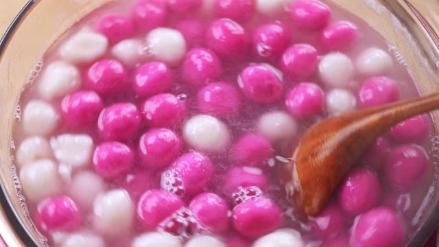 Boiling Tang yuan, tangyuan, delicious red and white rice dumpling balls in a glass pot. Concept of cooking at home for Winter Solstice, Chinese lantern Yuanxiao festival.