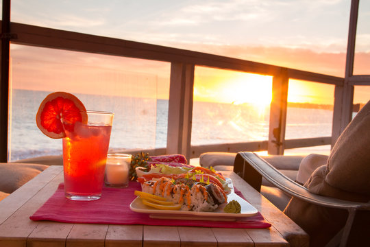 Oceanfront Dining At Sunset With Sushi Food And A Refreshing Drink On A Table