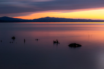 Obraz na płótnie Canvas Sunset a Trasimeno lake (Umbria, Italy), with fishing net poles and branches on perfectly still water
