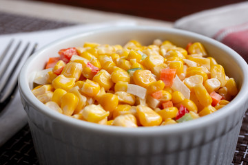 A closeup view of a ramekin bowl of Korean corn salad in a restaurant or kitchen setting.