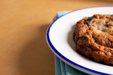 A view of chocolate chip cookie on a plate in a restaurant or kitchen setting, sitting on the right side of the frame.