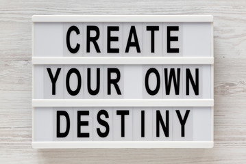 Obraz premium 'Create your own destiny' words on a lightbox on a white wooden background, top view. Overhead, from above, flat lay. Close-up.