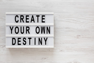 'Create your own destiny' words on a lightbox on a white wooden background, top view. Overhead, from above, flat lay. Copy space.