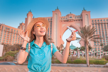 Tourist girl playing with toy white passenger airplane at the background of Hotel in Dubai sea resort. Concept of air travel and ticket prices