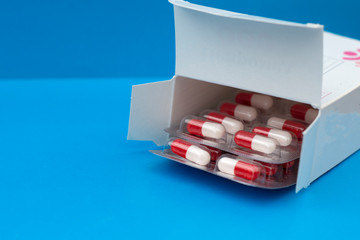 open box with white red capsules lying in it on a blue background