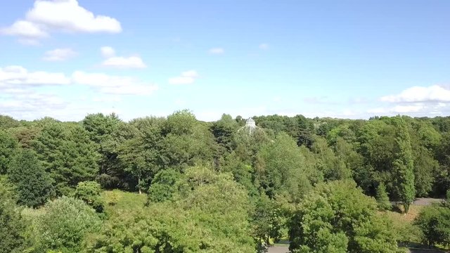 Accending drone shot above a park with a view of a beautiful greenhouse.