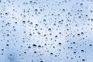 beautiful raindrops on glass window while raining with different texture with blue color blurred background.