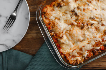Traditional Italian lasagna with vegetables, minced meat, tomatoes and cheese on a fabric and wooden background with wine