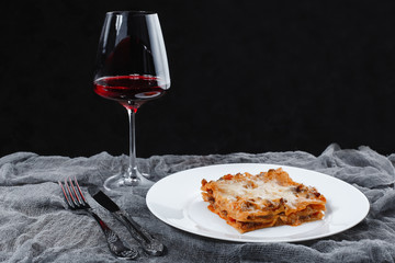 Traditional Italian lasagna with vegetables, minced meat, tomatoes and cheese on a fabric and wooden background with wine