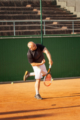 A bald man plays tennis on the court on a sunny day. Health and activity. Vertical.