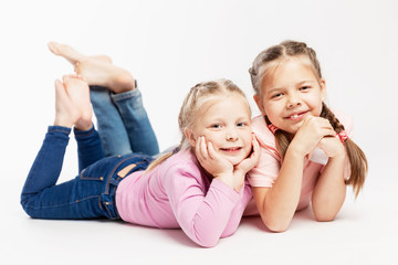 Two little girls are lying nearby and smiling. White background.