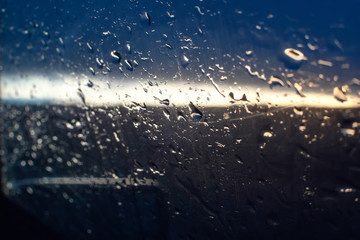 Raindrops on the side window of the car against the background of the sunset and the silhouette of a tree, a photo from inside the car