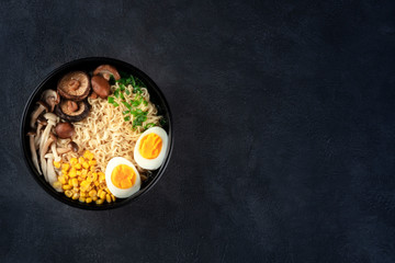 Ramen. Soba noodles with eggs, shiitake and enoki mushrooms, corn and scallions, top shot on a black background with a place for text