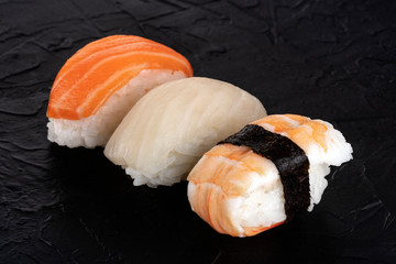 Nigiri sushi set, close-up on a black background. Fresh salmon, white fish, and shrimp on rice