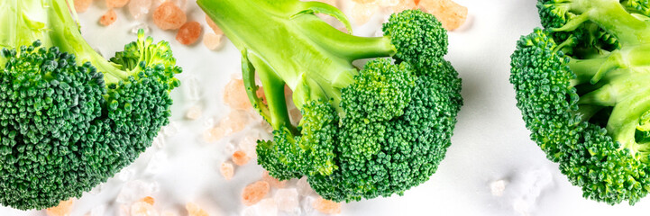 Broccoli florets close-up panoramic flat lay shot on a white background with pink Himalayan salt