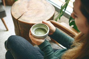 Girl drinks aromatic fresh and healthy green matcha latte tea in a cafe.