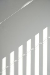 Light and shadows on a light wall through the window blinds. Diagonal parallel lines, abstract half frame composition. Copy space for text. Vertical.
