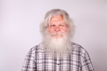 Senior thickset Caucasian happy man with splendid grey hair and beard on grey background. Attractive smile of elderly European handsome people close up. Beautiful portrait of grey-headed Santa Claus.