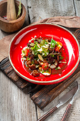 Warm beef liver salad with arugula, lettuce and tomatoes on a red plate. A delicious gourmet dinner in the rustic style