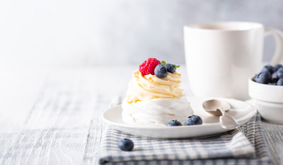 Delicious Pavlova cake with whipped cream and fresh berries. White cup of coffee. Selective focus