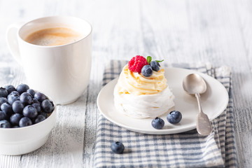 Delicious Pavlova cake with whipped cream and fresh berries. White cup of coffee. Selective focus