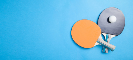 Table tennis rackets and a white plastic ball on a blue background.