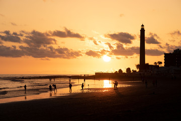 Fototapeta premium Figuras de personas a contraluz durante una puesta de sol dorada en la costa