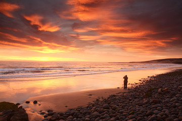 Fototapeta na wymiar Figura de una persona en la playa en un amanecer con nubes rojas