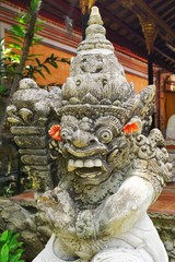 Fierce carved stone demon statue with red flowers in Bali Indonesia