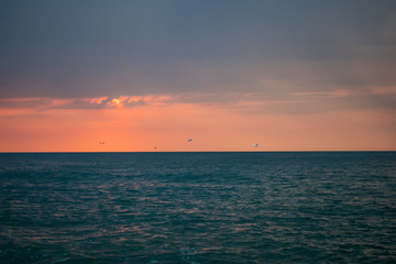 a beautiful sunset on the ocean. Boat and rocks near the shore. swans in flight