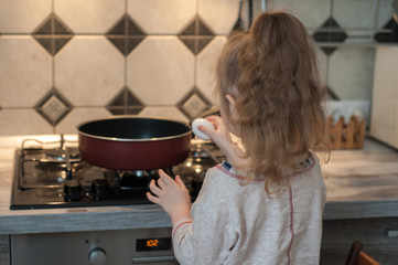 Little girl cooks fried eggs in a pan