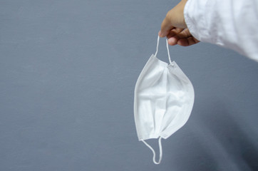 White surgical mask  in hand on grey background.
