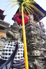 Looking up at a carved stone guardian statue wearing a checkered sarong outside a temple in Bali Indonesia