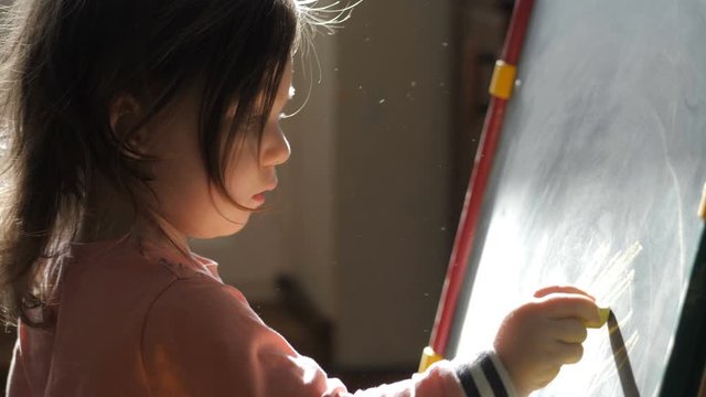 Curly cute little baby girl drawing with crayon color on the chalk board