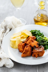 fried meat with potato chips and greens on white plate on ceramic background
