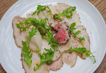 Sesame crusted tuna on smoked chicken ham and arugula salad leaves in white triangle plate top view