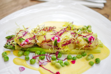 Seared scallops with cream sauce, shreded purple cabbage, green peas and asparagus in white triangle plate on wooden table