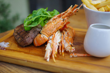 lobster and steak with french fries on wooden tray