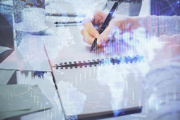 Hand taking notes in notepad. Forex chart holograms in front. Concept of research. Double exposure