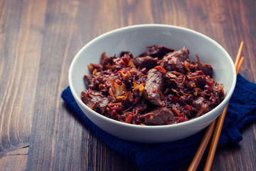 meat with vegetables in white bowl on brown wooden background