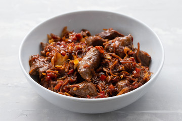 meat with vegetables in white bowl on ceramic background