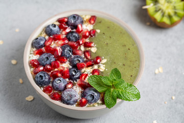 Green smoothie bowl with banana, kiwi, blueberry, granola and pomegranate. Healthy Breakfast detox cocktail in a bowl, vegan food. 