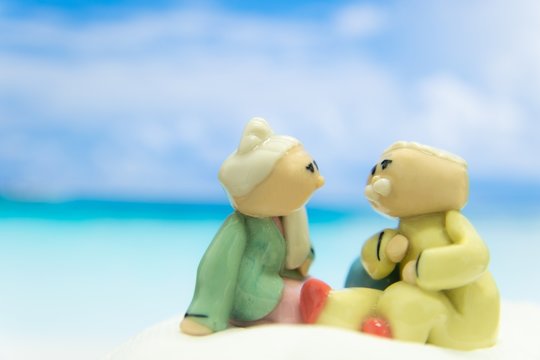 Happy Grandparents Couple Looking To Each Other. They Sat On The Beach Against The Blue Sky With Clouds. In Concept A Long And Lasting Love.