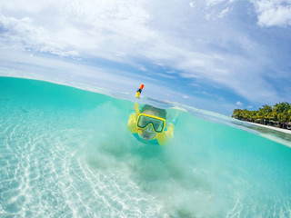 Split underwater photo of child in mask snorkeling in blue ocean water near tropical island