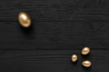 Golden eggs on black wooden background. Making money, savings, pensions and successful investment concept, top view, copy space