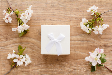 Gift box with cherry flowers on the wooden background.