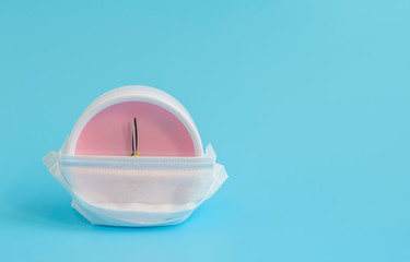 alarm clock in a protective respiratory mask on a blue background, concept of colds and viruses, copy space